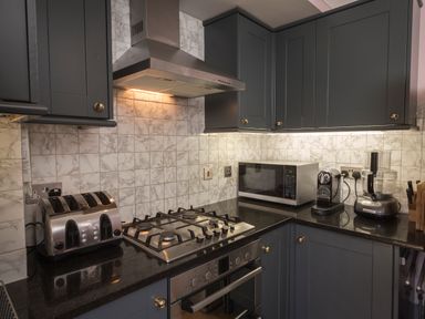 A kitchen with grey cabinets a gas stove a stainless steel toaster microwave coffee maker and food processor at 16 Courtenay Street in Salcombe