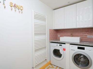 A laundry room with a washing machine a dryer a sink white cabinets and pink tiled backsplash at 16 Courtenay Street in Salcombe