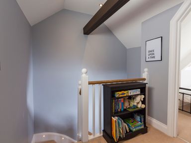 A staircase landing with a black bookshelf containing books and toys at 16 Courtenay Street in Salcombe