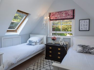 A bedroom with two single beds a black chest of drawers between them a window with a pink patterned blind and a skylight window at 16 Courtenay Street in Salcombe