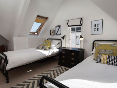 A bedroom with two single beds black metal frames a black chest of drawers with two lamps and two windows at 16 Courtenay Street in Salcombe