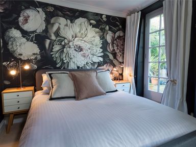 A bedroom with a large floral mural on the wall white bedding bedside tables with lamps and glass doors with curtains at 16 Courtenay Street Salcombe