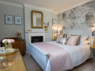 A bedroom with a bed a fireplace a mirror and floral decorations at 16 Courtenay Street in Salcombe