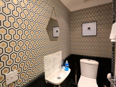 A small bathroom with a toilet sink soap dispenser hexagonal mirror and patterned wallpaper at 16 Courtenay Street in Salcombe