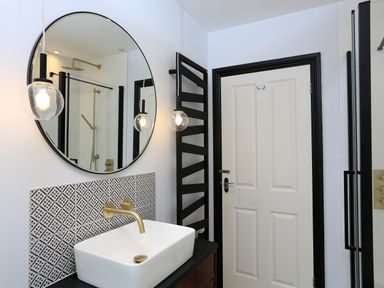 A bathroom with a white sink and brass faucet under a round mirror with two hanging light bulbs and a white door with black frame at 16 Courtenay Street in Salcombe