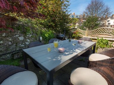 An outdoor patio dining area with a rectangular table surrounded by wicker chairs and drinks on the table at 16 Courtenay Street in Salcombe