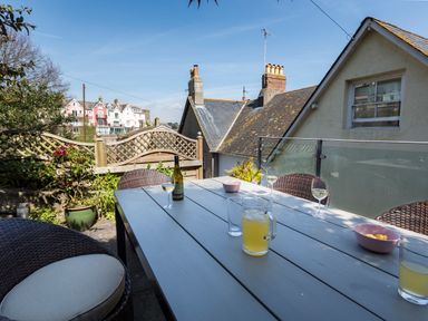 An outdoor patio with a table and chairs glasses and drinks on the table overlooking neighboring rooftops at 16 Courtenay Street in Salcombe