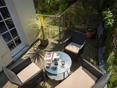 An outdoor patio with four wicker chairs around a glass table with cups and a magazine at 16 Courtenay Street in Salcombe