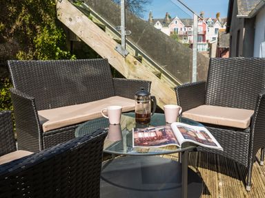 An outdoor seating area with wicker chairs and sofa around a glass table with a coffee press two mugs and an open magazine at 16 Courtenay Street in Salcombe