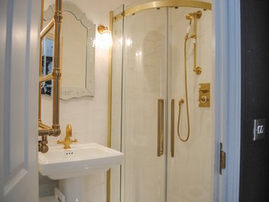 A bathroom with a white pedestal sink and gold fixtures next to a glass shower enclosure with gold trim at 16 Courtenay Street in Salcombe