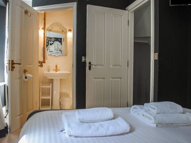 A bedroom with white towels on the bed and an open door showing a bathroom with a pedestal sink and mirror at 16 Courtenay Street in Salcombe