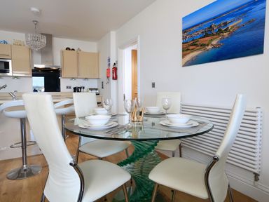 A kitchen and dining area with a glass round table and white chairs at 1 At The Beach in Torcross