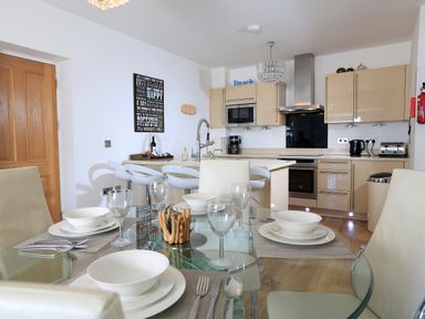 A kitchen with a glass dining table set with bowls and glasses at 1 At The Beach in Torcross
