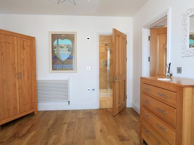 A bedroom with wooden wardrobe wooden chest of drawers an open wooden door leading to a bathroom and a framed picture on the wall at 1 At The Beach in Torcross