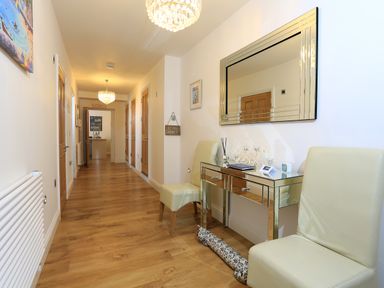 A hallway with wooden floor two cream chairs a mirrored console table a large mirror and multiple wooden doors at 1 At The Beach in Torcross