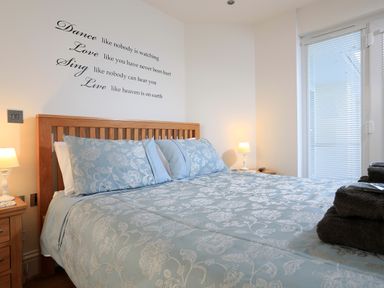 A bedroom with a wooden bed frame blue floral bedding bedside tables lamps and a glass door with blinds at 1 At The Beach in Torcross