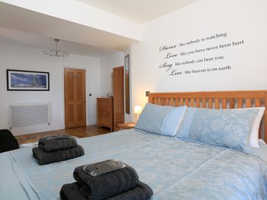 A bedroom with a large bed with blue bedding wooden furniture and a wall decal at 1 At The Beach in Torcross