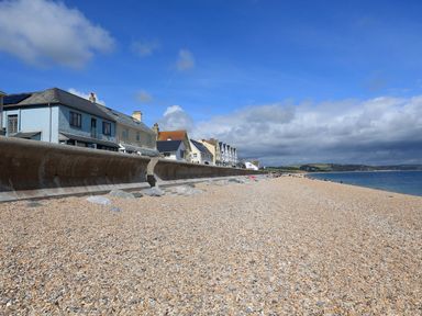 A pebble beach with a concrete sea wall and houses along the shoreline at 1 At The Beach in Torcross