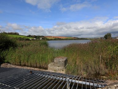 A lake surrounded by reeds and grass with hills and houses in the background at 1 At The Beach in Torcross
