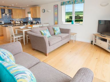 An open-plan living room and kitchen with sofas, dining table, kitchen cabinets, and a television at 2 Ocean's Edge in Thurlestone