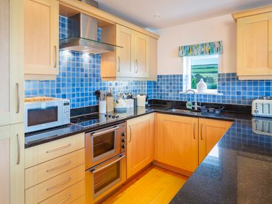 A kitchen with wooden cabinets black countertops and blue tiled backsplash at 2 Ocean's Edge in Thurlestone