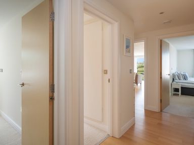 A hallway with three open doors showing a bedroom and a dining area at 2 Ocean's Edge in Thurlestone