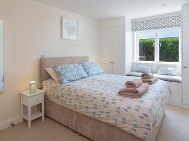 A bedroom with a bed with patterned bedding and towels on top next to a window seat with cushions at 2 Ocean's Edge in Thurlestone