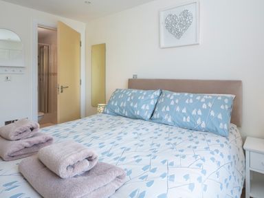 A bedroom with a bed with pillows and folded towels an open door showing a bathroom at 2 Oceans Edge in Thurlestone