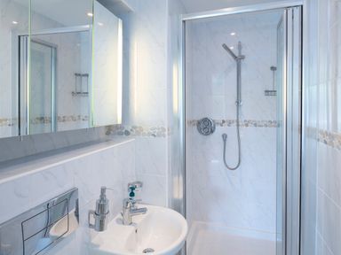 A bathroom with a sink a mirror soap dispenser and a shower cubicle at 2 Ocean's Edge in Thurlestone