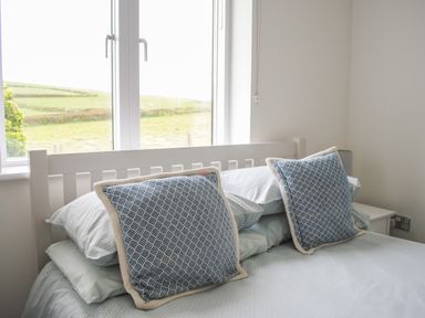 A bed with two blue patterned cushions in front of a window and a bedside table at 2 Ocean's Edge Thurlestone