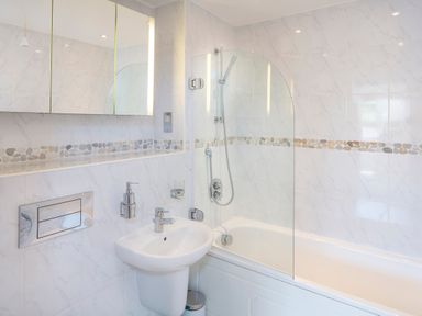 A bathroom with a sink, bathtub with shower, and mirrored cabinets above the sink at 2 Ocean's Edge in Thurlestone