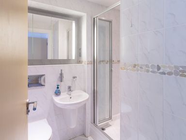 A bathroom with a sink soap dispenser shower cubicle and a wall-mounted mirror at 2 Ocean's Edge in Thurlestone
