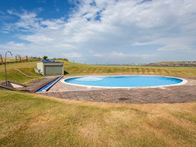 An outdoor round swimming pool with stone paving and grassy lawn surrounding it at 2 Ocean's Edge in Thurlestone