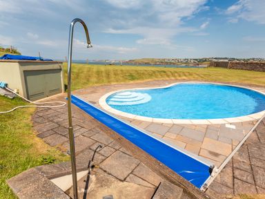 An outdoor swimming pool with steps and a shower beside a grassy area near the coast at 2 Ocean's Edge in Thurlestone