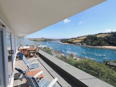 A balcony with wooden chairs and table overlooking a river with boats and hills in the background at 2 Poundstone Court in Salcombe