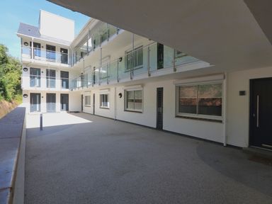 An open courtyard of a multi level building with glass railings and several doors and windows at 2 Poundstone Court in Salcombe