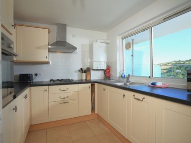 A kitchen with cream cabinets black countertops a gas stove a sink under a window overlooking hills at 2 Poundstone Court in Salcombe