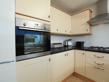 A kitchen with cream cabinets black countertop built-in oven stove toaster kettle scale and bread bin at 2 Poundstone Court in Salcombe