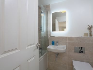A bathroom with a sink, illuminated mirror, partially open door, glass shower enclosure, and toilet at 2 Poundstone Court in Salcombe