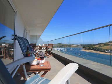 A balcony with chairs, a table with wine and snacks, overlooking a river with boats and hills at 2 Poundstone Court in Salcombe