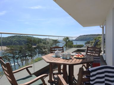 A balcony with wooden table and chairs overlooking a body of water and trees at 2 Poundstone Court in Salcombe