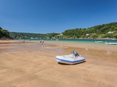 A beach with a small inflatable boat on sand and people walking near the water at 2 Poundstone Court in Salcombe