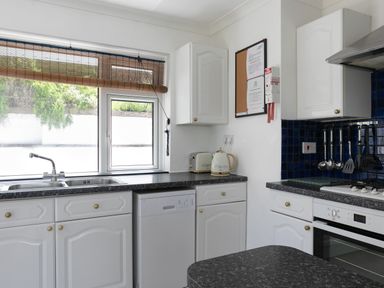 A kitchen with white cabinets a window with a blind a toaster a kettle a stove and hanging kitchen utensils at 2 Rockmount in Salcombe