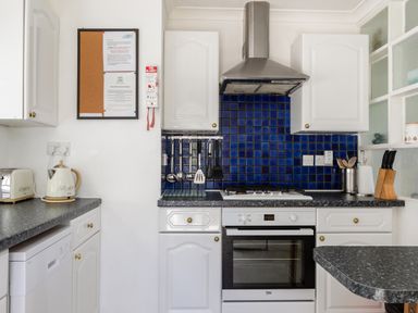 A kitchen with white cabinets a stove oven blue tiled backsplash and utensils at 2 Rockmount in Salcombe
