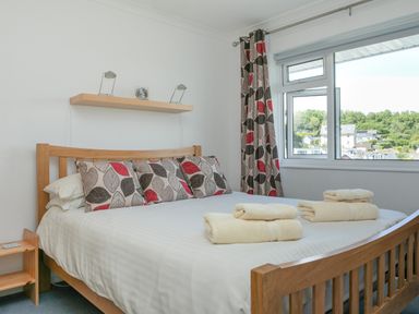 A bedroom with a wooden bed and leaf patterned cushions and curtains at 2 Rockmount in Salcombe