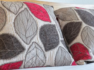 Two cushions with leaf pattern in red gray and beige colors on a bed at 2 Rockmount in Salcombe