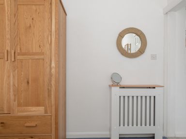A wooden wardrobe next to a white radiator cover with a small round mirror on top and a round rope-framed mirror on the wall at 2 Rockmount in Salcombe