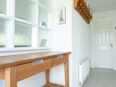 A hallway with a wooden table below frosted glass panels a white door a radiator and a wooden coat rack with hooks at 2 Rockmount in Salcombe