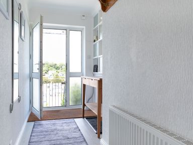 A hallway with a wooden table a radiator a purple rug and an open glass door at 2 Rockmount in Salcombe