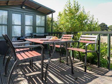 An outdoor wooden deck with a table and chairs next to a green building at 2 Rockmount in Salcombe